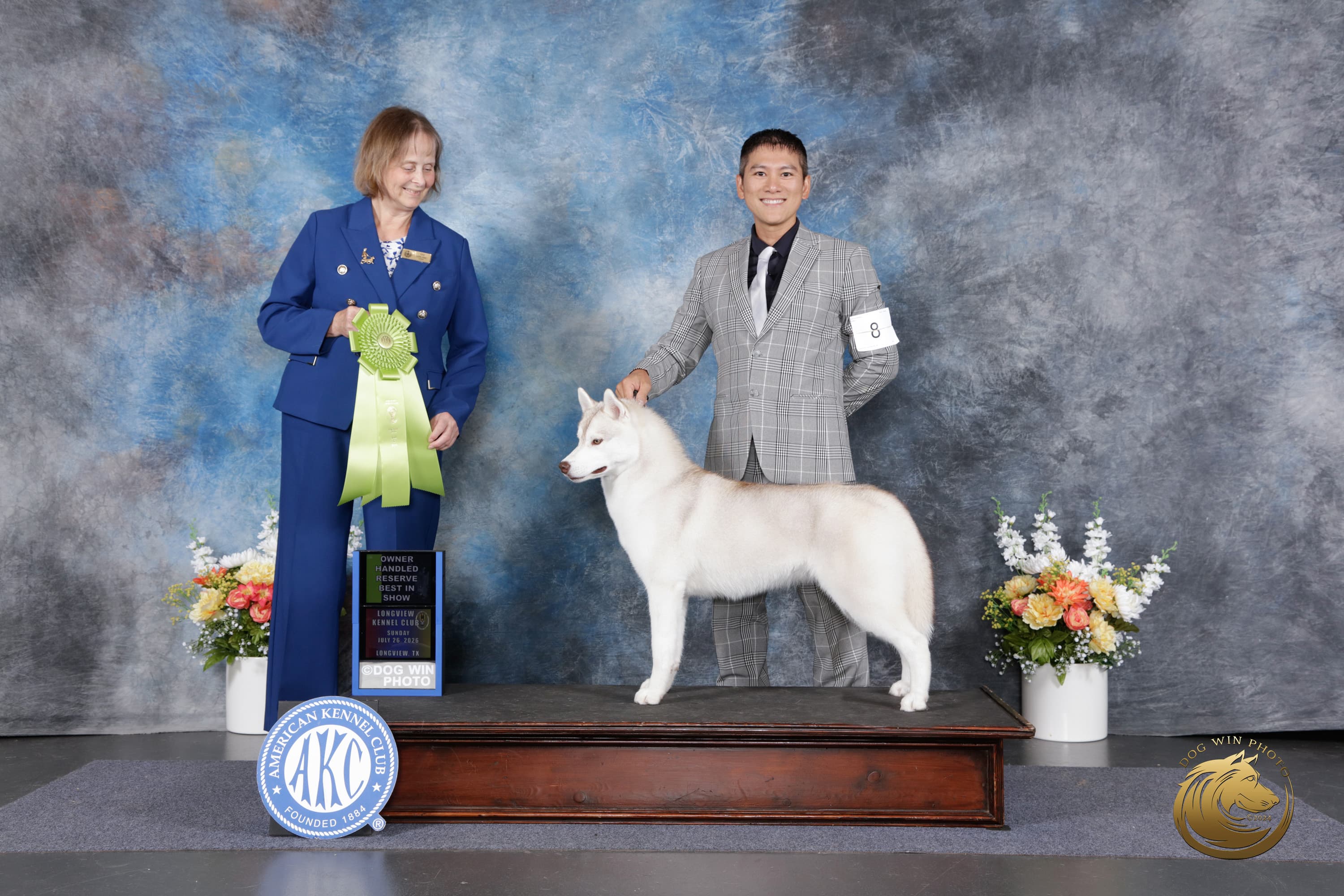 Caramel posed with her handler and Judge Kim LeBlanc beside a green Owner-Handled Reserve Best in Show ribbon at Longview Kennel Club in 2026