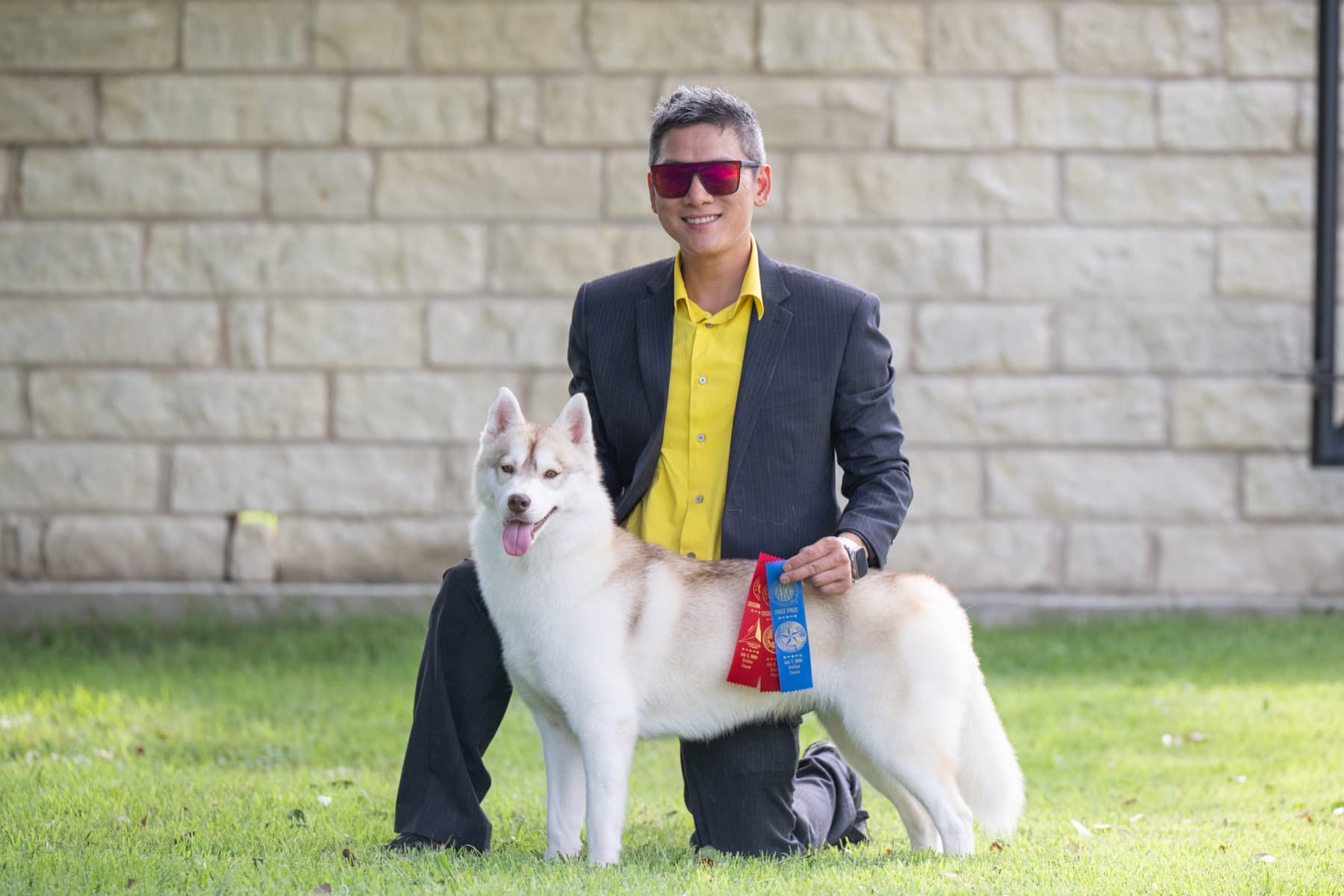 Pumpkin posed outdoors beside her handler with red and blue show ribbons